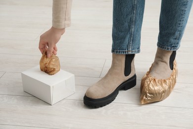 Photo of Woman wearing shoe covers onto her boots indoors, closeup