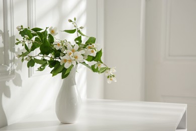 Photo of Beautiful bouquet with fresh jasmine flowers in vase on white table indoors, space for text