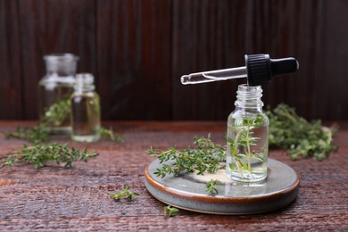 Photo of Thyme essential oil and fresh plant on wooden table, space for text