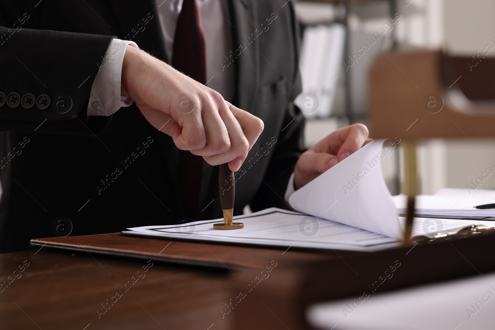 Photo of Notary stamping document at wooden table in office, closeup
