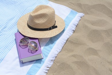 Beach towel with book, sunglasses and straw hat on sand, space for text