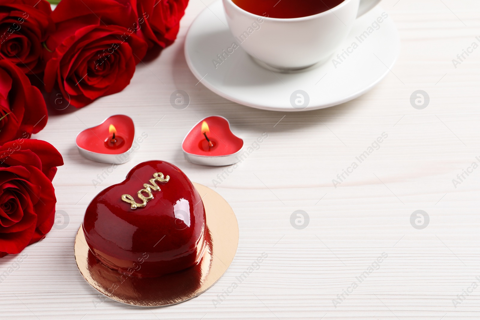 Photo of St. Valentine's Day. Delicious heart shaped cake, tea, roses and candles on white wooden table. Space for text