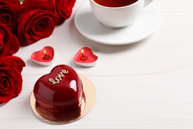 Photo of St. Valentine's Day. Delicious heart shaped cake, tea, roses and candles on white wooden table. Space for text