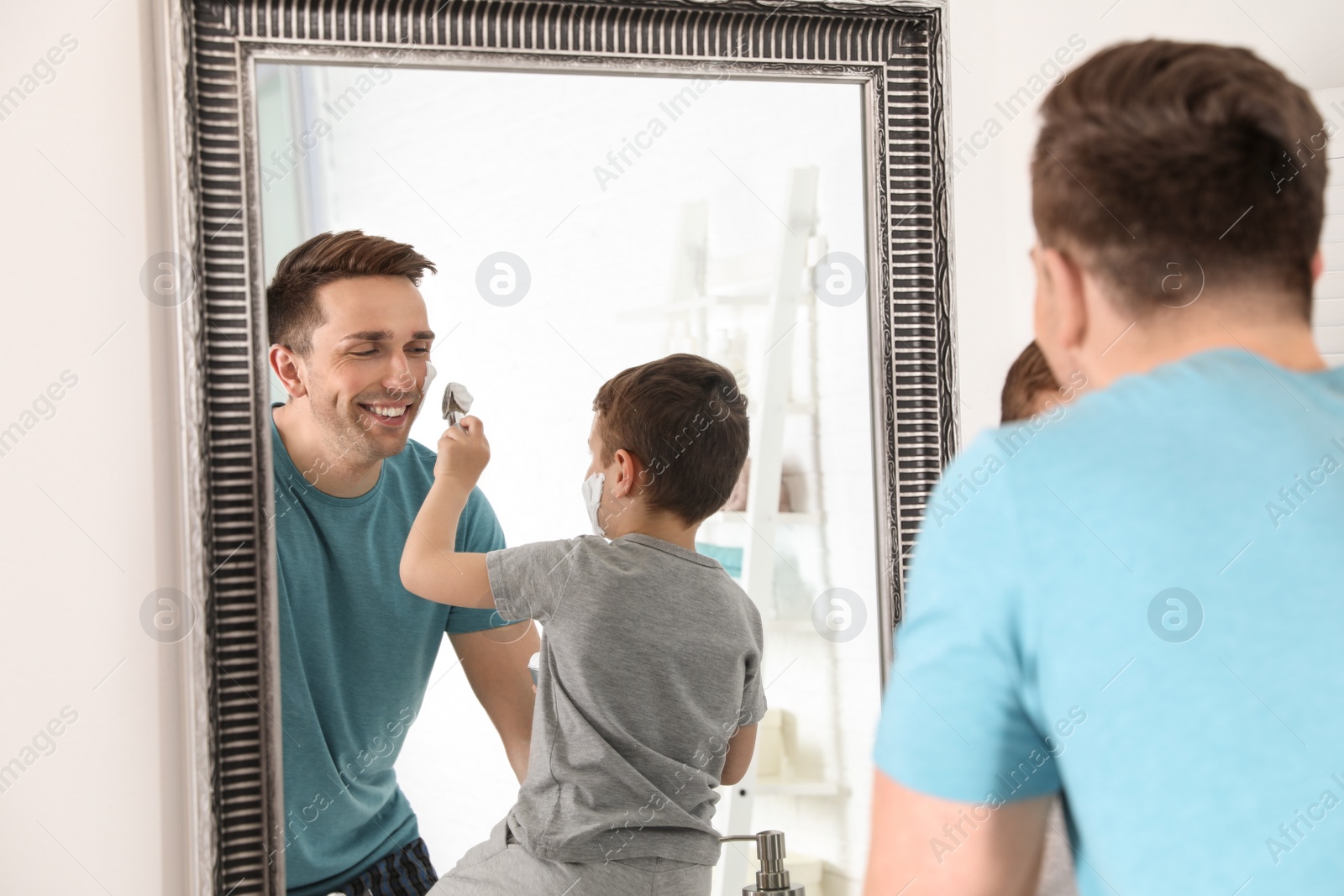 Photo of Little son applying shaving foam onto dad's face in bathroom