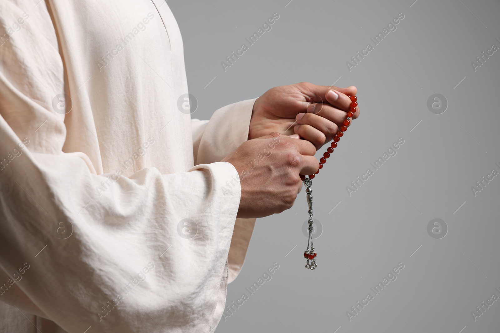 Photo of Muslim man with misbaha on light grey background, closeup