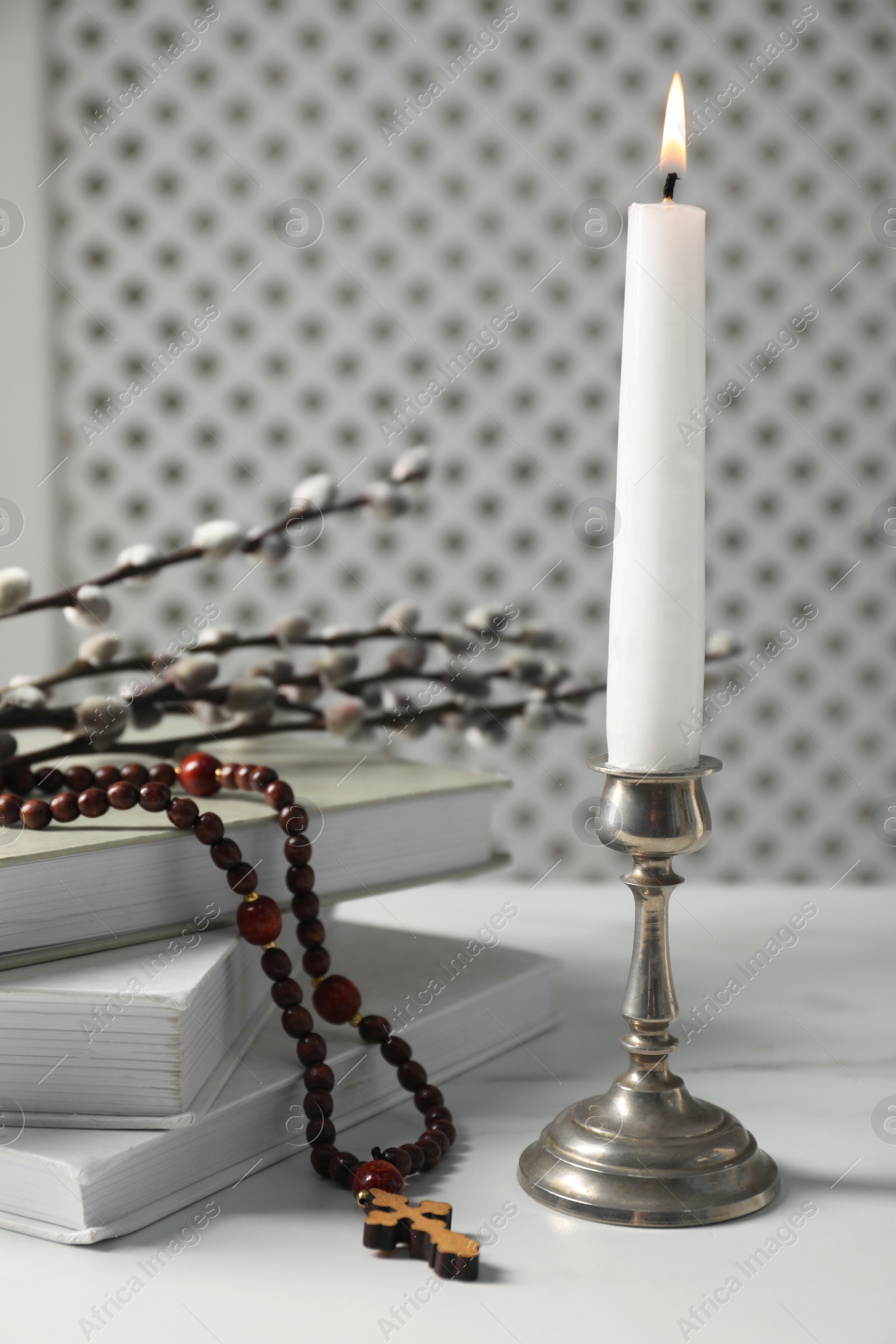 Photo of Books, burning candle, rosary beads and willow branches on white marble table, closeup