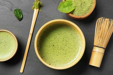 Photo of Fresh matcha tea, bamboo whisk, spoon and green powder on black table, flat lay