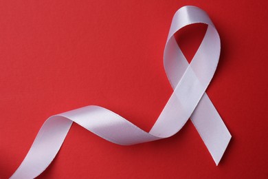 Photo of White awareness ribbon on red background, top view. Space for text