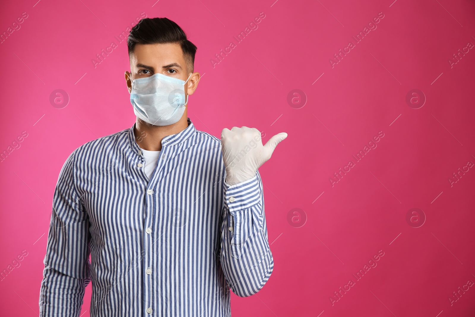 Photo of Man in protective face mask and medical gloves pointing at something on pink background. Space for text