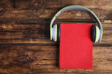 Photo of Book and modern headphones on wooden table, top view. Space for text