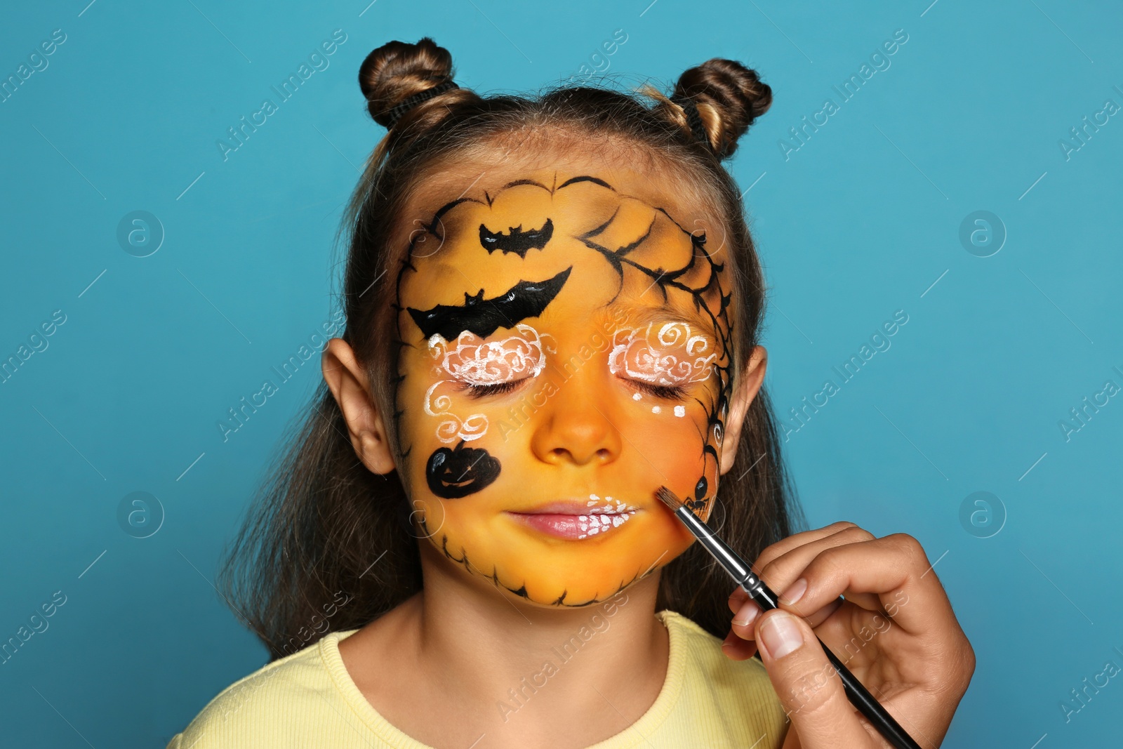 Photo of Artist painting face of little girl on blue background