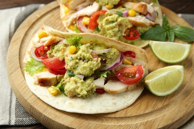Delicious tacos with guacamole, meat and vegetables served with lime on table, closeup