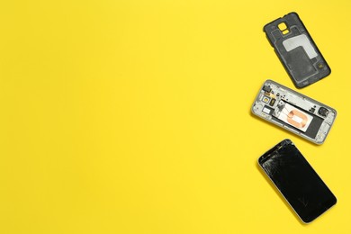 Photo of Damaged smartphone on yellow background, flat lay with space for text. Device repairing