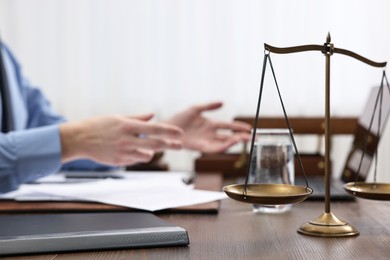 Photo of Lawyer working at wooden table, focus on scales of justice