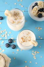 Tasty yogurt in glasses, oats, banana and blueberries on light blue wooden table, flat lay