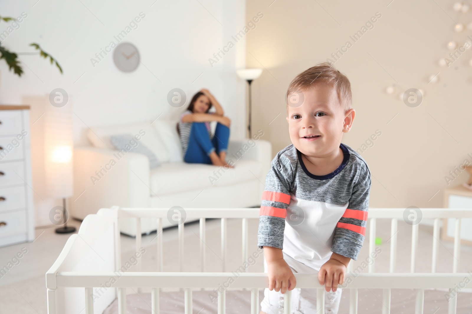 Photo of Cute baby boy in crib and young mother suffering from postnatal depression on blurred background