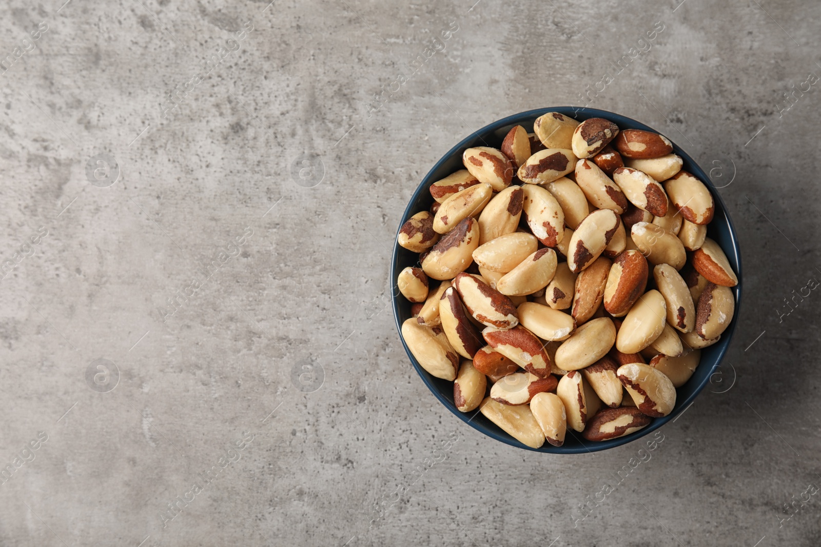 Photo of Bowl with tasty Brazil nuts and space for text on grey background, top view