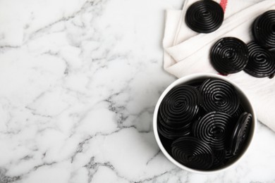 Photo of Tasty black liquorice candies on white marble table, flat lay. Space for text