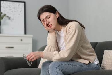 Overwhelmed woman with glasses sitting on sofa at home