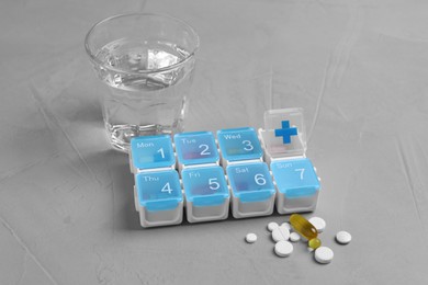 Weekly pill box with medicaments and glass of water on grey table