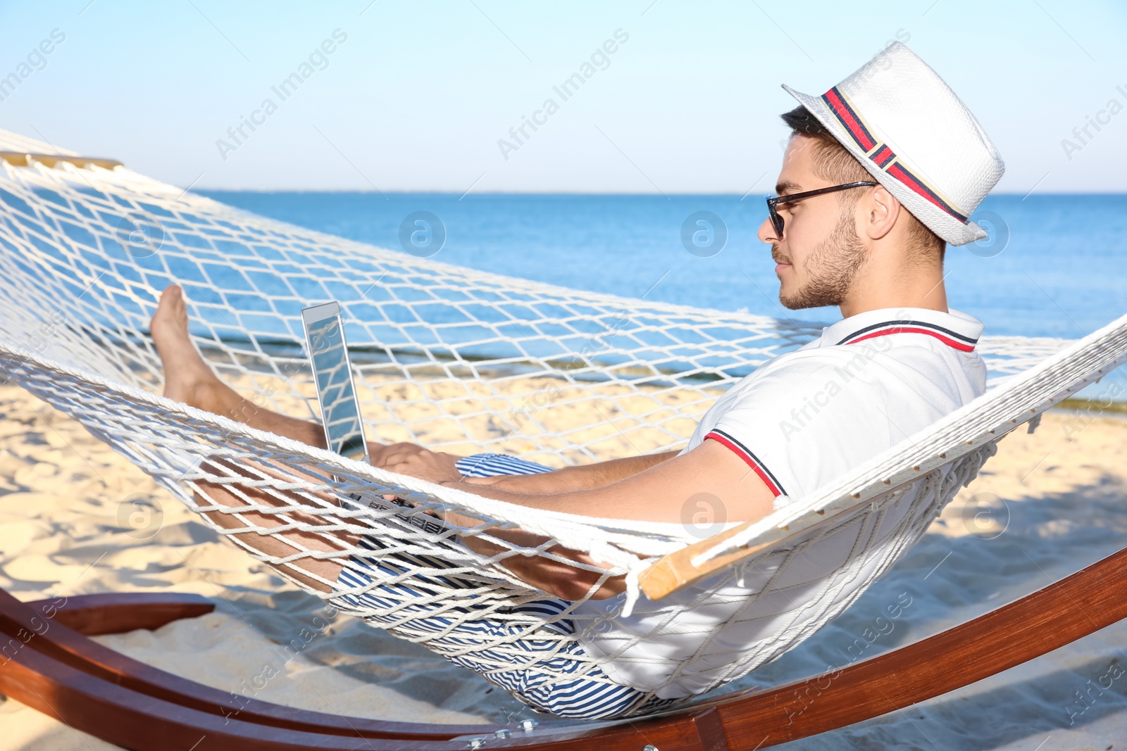 Photo of Young man with laptop resting in hammock at seaside