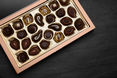 Photo of Box of delicious chocolate candies on black table, top view. Space for text