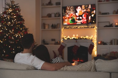 Photo of Couple watching Christmas movie via TV in cosy room, back view. Winter holidays atmosphere