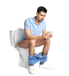 Photo of Emotional man with smartphone sitting on toilet bowl, white background