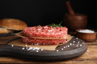 Photo of Raw hamburger patties with rosemary and spices on wooden table, closeup