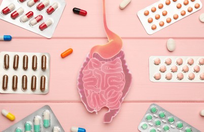 Photo of Paper cutout of small intestine and pills on pink wooden background, flat lay