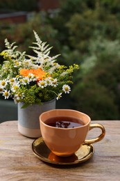 Cup of delicious chamomile tea and fresh flowers outdoors