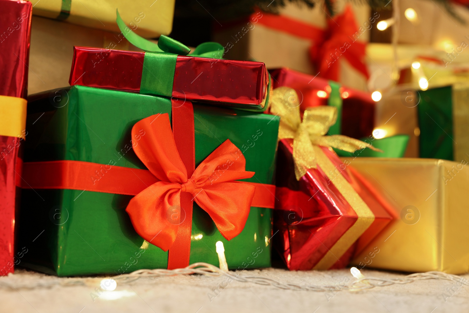 Photo of Many different gift boxes and festive lights on carpet, closeup. Christmas celebration