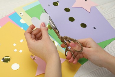 Photo of Woman cutting paper heart with scissors at white wooden table, closeup