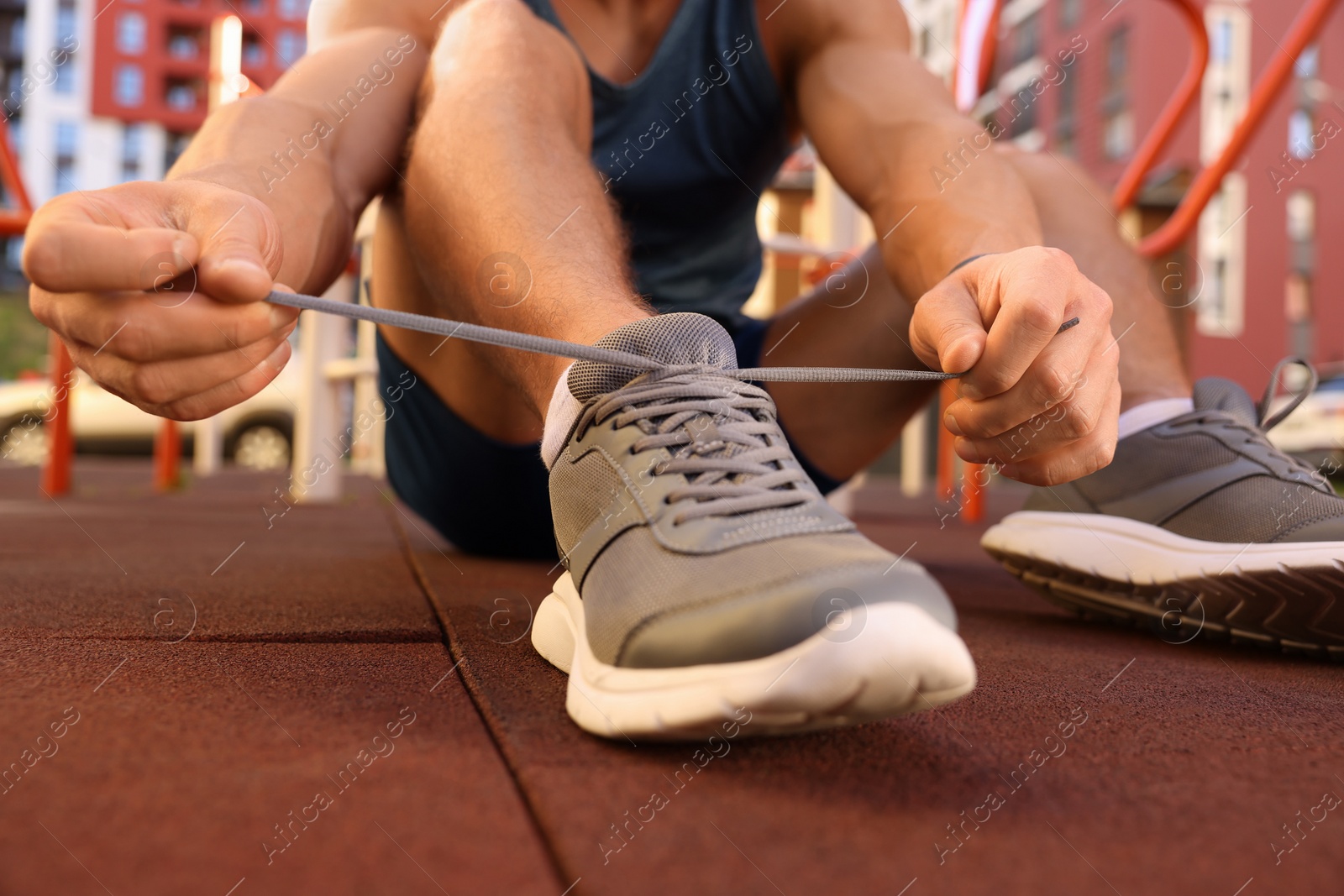 Photo of Man tying shoelaces before training at outdoor gym, closeup