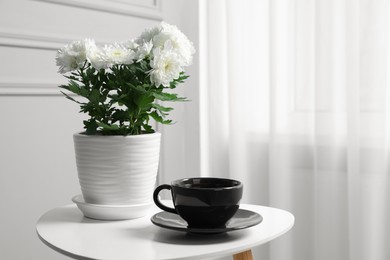 Photo of Beautiful chrysanthemum flowers in pot and cup of drink on white table indoors