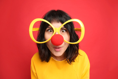 Photo of Funny woman with large glasses and clown nose on red background. April fool's day