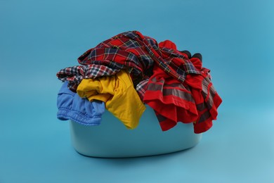 Laundry basket overfilled with child clothes on light blue background