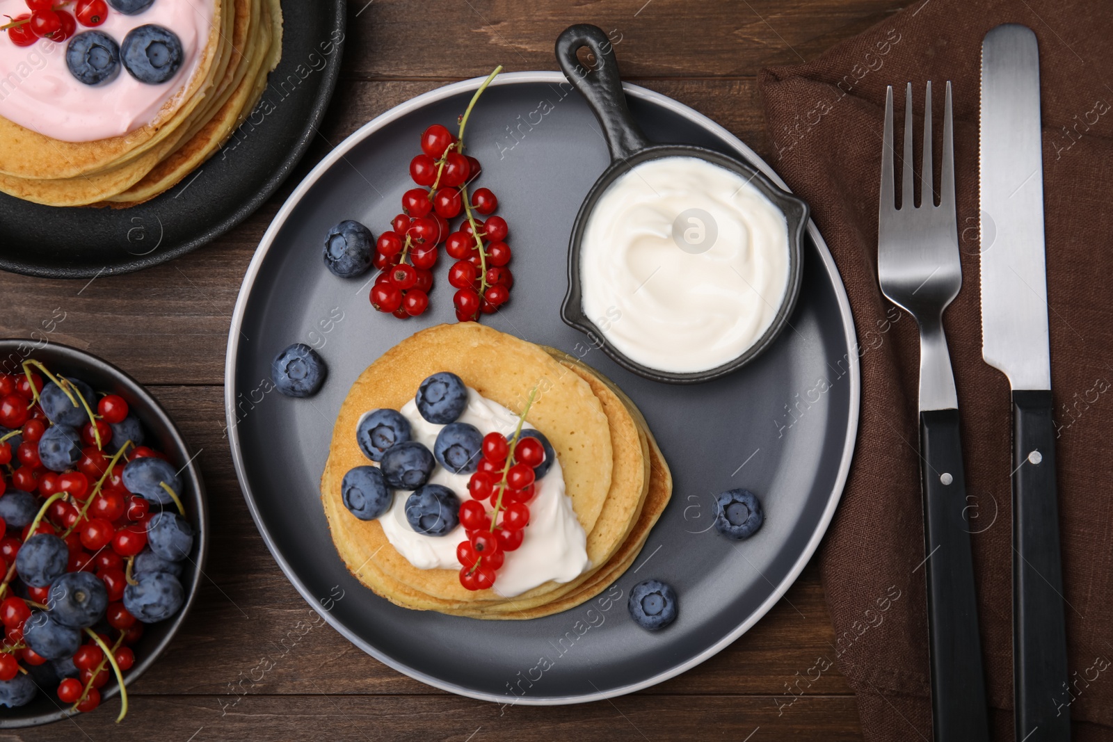 Photo of Tasty pancakes with natural yogurt, blueberries and red currants on wooden table, flat lay