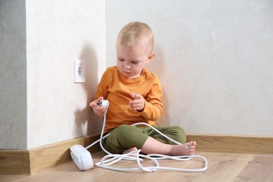 Photo of Little child playing with power strip plug near electrical socket at home. Dangerous situation