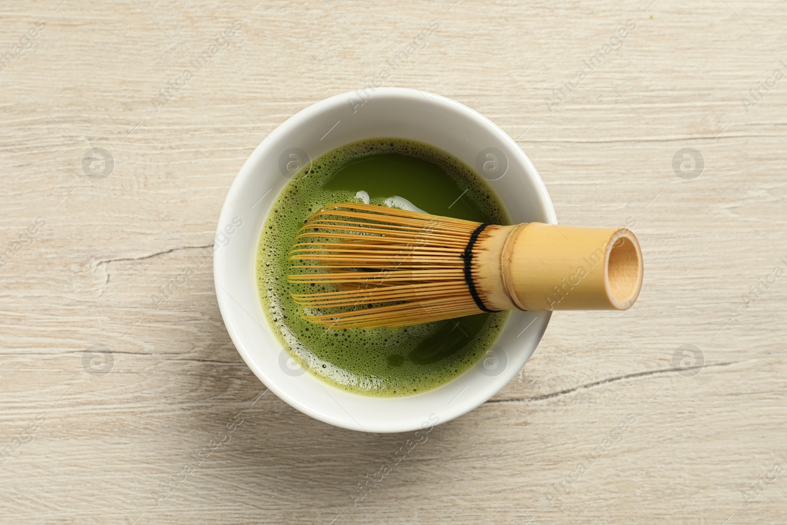 Photo of Cup of fresh green matcha tea with bamboo whisk on wooden table, top view
