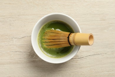 Cup of fresh green matcha tea with bamboo whisk on wooden table, top view