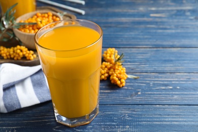 Photo of Sea buckthorn juice on blue wooden table, closeup. Space for text