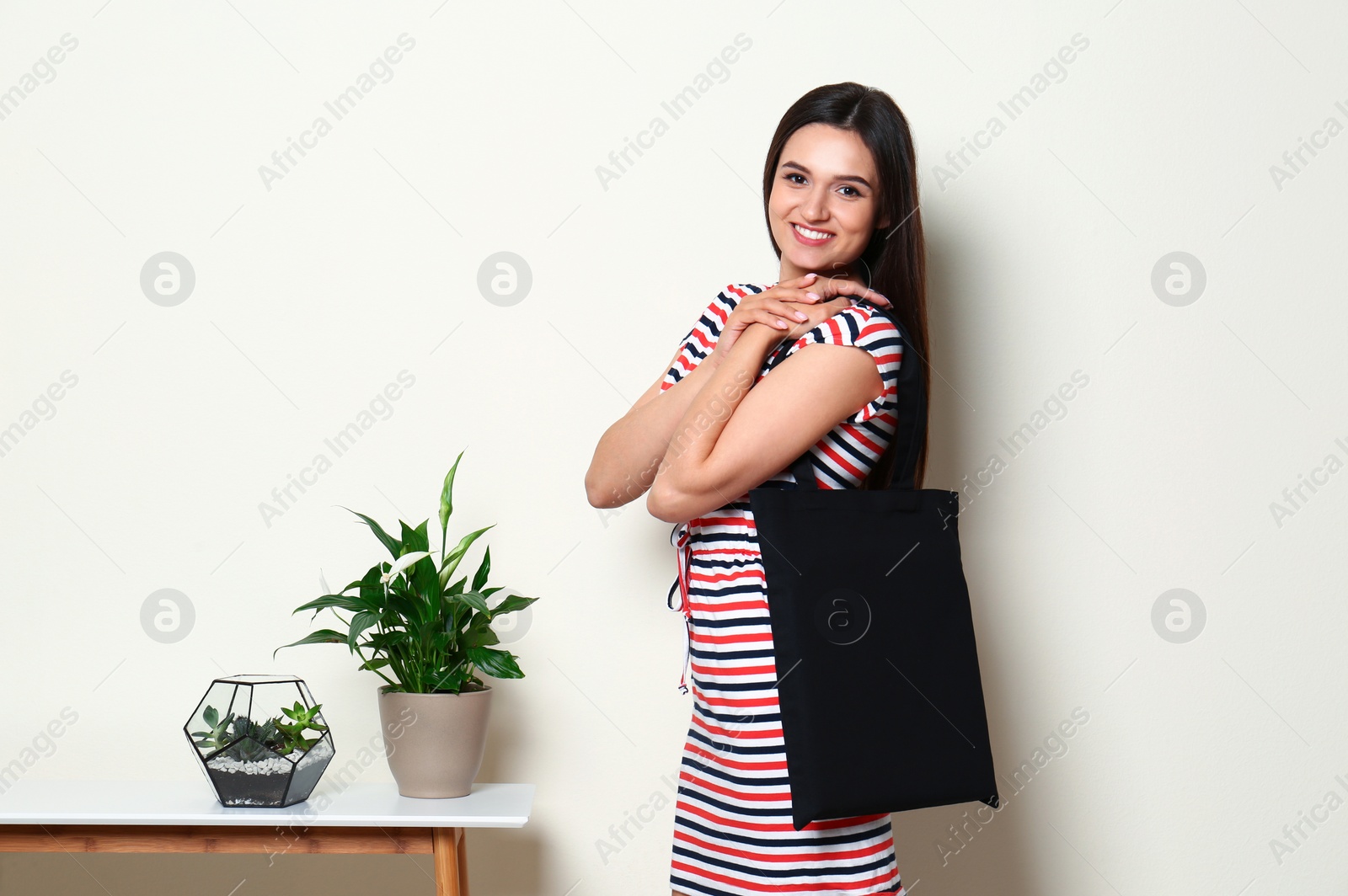 Photo of Beautiful young woman with stylish blank eco bag near white wall
