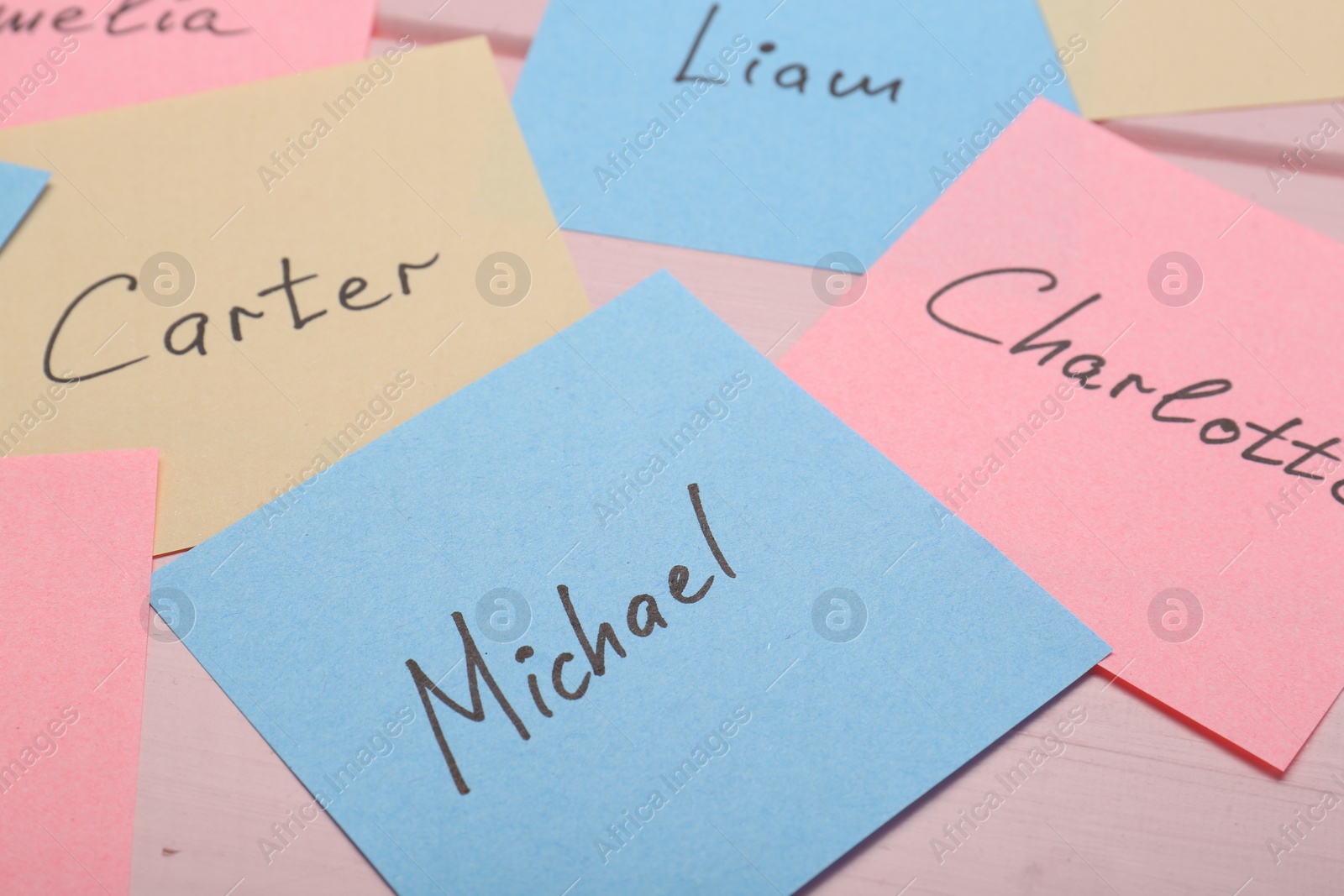 Photo of Paper stickers with different names on pink wooden table, closeup. Choosing baby's name