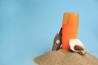 Photo of Sand with bottle of sunscreen, tree bark and seashells against light blue background, space for text. Sun protection