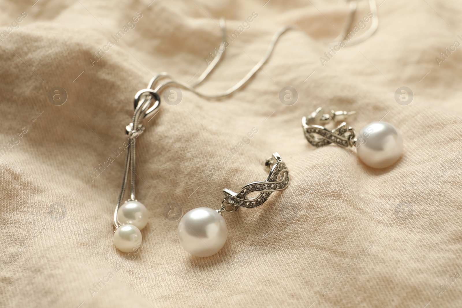 Photo of Elegant necklace and silver earrings with pearls on beige fabric, closeup