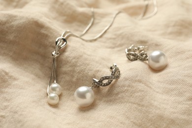 Elegant necklace and silver earrings with pearls on beige fabric, closeup