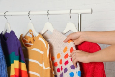 Photo of Woman choosing sweater on rack against brick wall, closeup