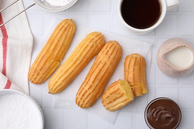 Delicious eclairs, chocolate paste and coffee on white checkered table, flat lay