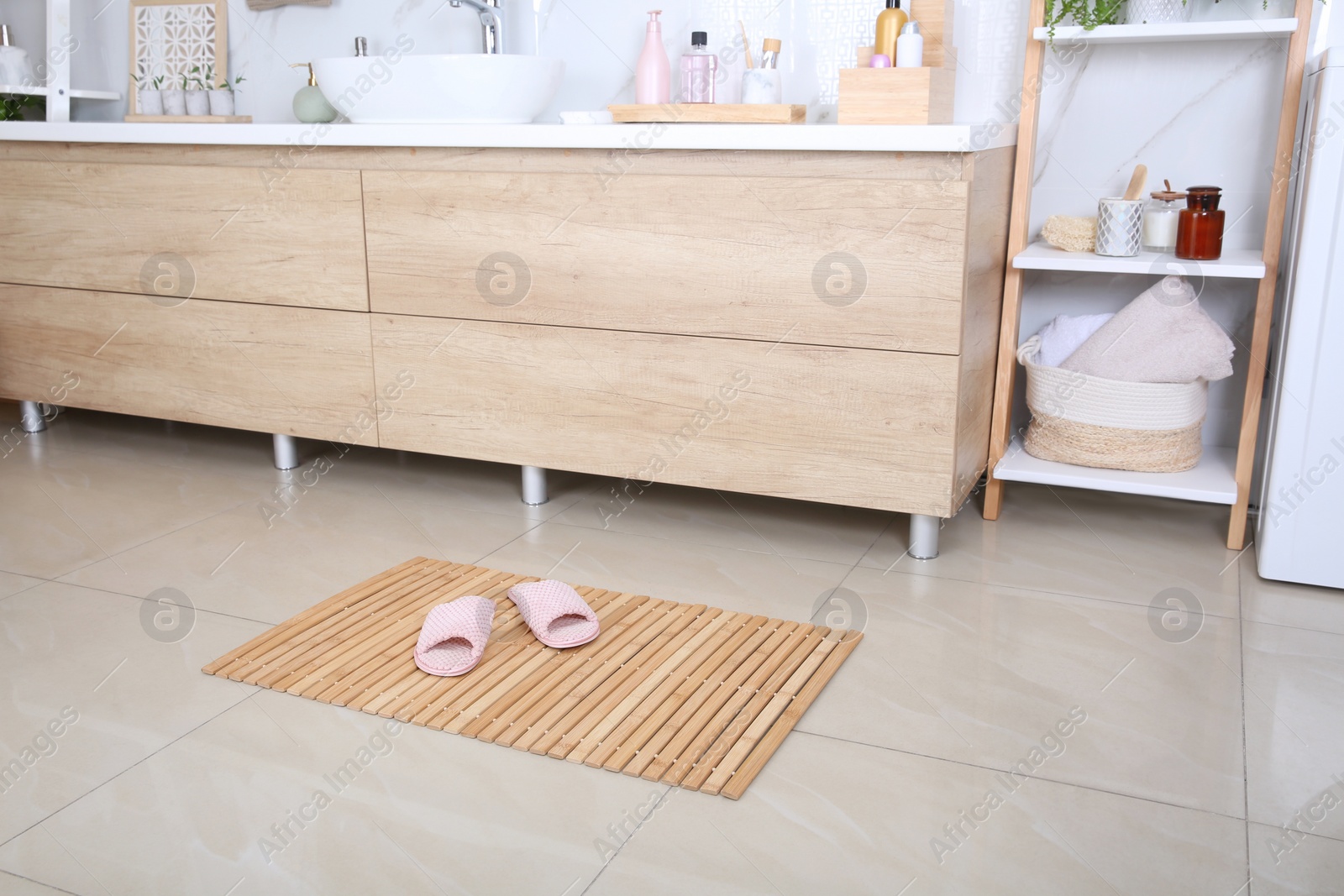 Photo of Wooden mat with slippers on floor in bathroom